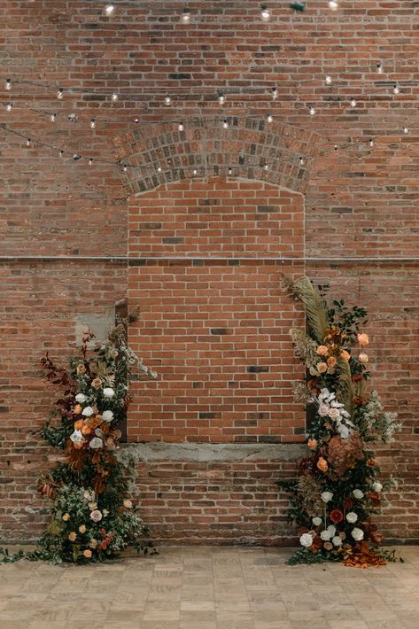 Wedding Brick Wall Decor, Brick Wall Floral Backdrop, Brick Wedding Ceremony, Exposed Brick Wedding Decor, Dried Flower Arch Wedding, Earth Tone Spring Wedding, Earth Tone Flower Arrangements, Fall Wedding Alter Decor, Floral Columns Wedding