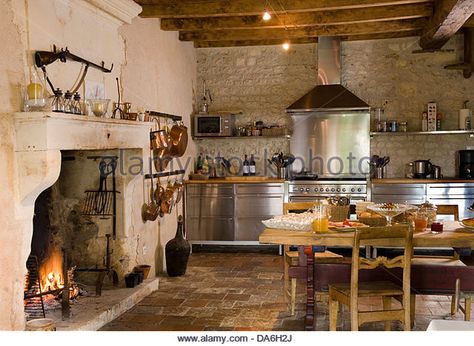 Lit fire in fireplace in country kitchen with rustic wooden table and chairs stainless steel fitted units - Stock Image Vintage Kitchen With Fireplace, Cooking Fireplace In Kitchen, Country Kitchen With Fireplace, Stone Fireplace In Kitchen, Fireplace Kitchen Ideas, Kitchen Fireplace Cooking, Kitchen Fireplace Ideas, Fire In Fireplace, Fireplace In Kitchen