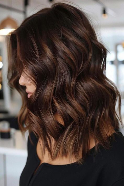 Woman with wavy, shoulder-length brown hair wearing a black top in a well-lit room. Chestnut Lowlights Brunettes, Dark Brown Hair With Amber Highlights, Full Color Hair Ideas Brown, Brunette Hair Color With Highlights Caramel, Short Dark Brown Hair With Caramel Highlights, Warm Brown Highlights On Dark Hair, Medium Length Dark Brown Hair Balayage, Short Hair Caramel Highlights, Highlights Color Ideas