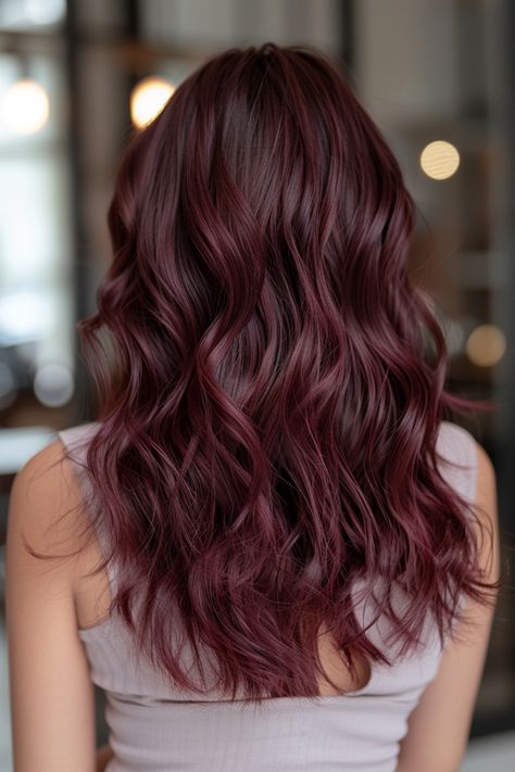 Woman with long, wavy, burgundy hair stands indoors, facing away from the camera. Mid Length Hair Color Ideas Brunettes, Cherry Brown Balayage Brunettes, Ruby Brown Hair, Brown Hair With Cherry Cola Highlights, Cherry Cola Hair With Highlights, Brown Hair With Burgundy, Cherry Mocha Hair, Cherry Cola Hair Color Brunettes, Brown Hair With Burgundy Highlights