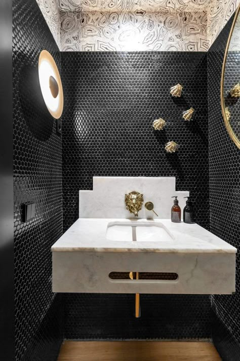 This sophisticated powder room in Spain features black penny tile-covered walls and marble vanity with a gold faucet that looks like a lion’s head. Powder Room Tile, Penny Tiles Bathroom, Black Powder Room, Beautiful Powder Rooms, Luxury Powder Room, Penny Tile Floors, Contemporary Powder Room, Powder Room Ideas, Penny Tile