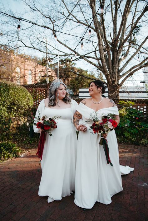 Two brides pose for their couple portraits at LGBTQI+ wedding wearing wedding dresses with trains holding white and deep red winter wedding bouquets | bridal bouquets | winter bride | winter wedding fashion | Three Region Photography Bridal Bouquets Winter, Red Winter Wedding, Christmas Winter Wedding, Bride Winter, Winter Wedding Red, Winter Wedding Fashion, Winter Floral Arrangements, White Winter Wedding, Queer Weddings