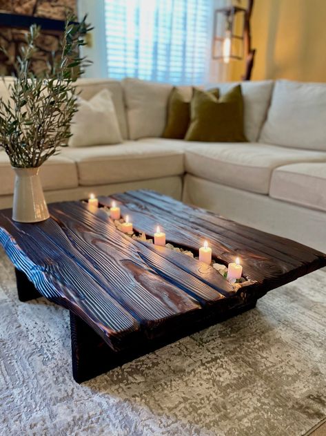 38"L x 30"W x 12"H (Ask for a custom size) Our Venezia Coffee Table is a charismatic rustic centerpiece that features faux live edges to imitate a beautiful slab design from douglas fir lumbers. Its deep black carbon finish, induced through the ancient Japanese wood-burning technique Shou Sugi Ban, pairs nicely with its elegant slender frame. Furthermore, the rectangular top has a carved river in the middle which you can garnish and style freely. *Candles and pebbles not included* Painting On Coffee Table, Giant Coffee Table, Rustic Home Furniture, Rustic Coffee Table Ideas, Middle Table Living Room, Dark Rustic Living Room, Unique Coffee Table Ideas, Dark Coffee Table, Homemade Coffee Tables