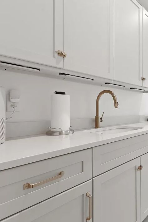 This clean design laundry room is a dream come true for anyone who loves a touch of elegance in their chores. Crisp white cabinets with bronze hardware create a sophisticated feel, while a sparkling white quartz countertop adds a touch of glamour.  A  white porcelain sink keeps things bright and airy. This functional space is both stylish and efficient, making laundry day a breeze. #laundryroomgoals #quartzlaundry #bronzedetails #luxuryhome #whiterूम #laundryinspo #lavanderíalujosa #blancototal Black White Gold Laundry Room, White Gold Laundry Room, White Cabinets With Bronze Hardware, Gold Laundry Room, Sparkling White Quartz Countertop, White Laundry Room, Sparkling White Quartz, Elegant Laundry Room, Narrow Laundry Room