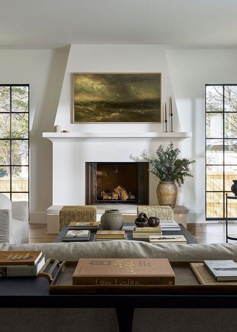 A Samsung Frame TV hangs over a white plaster fireplace mantel finished with a hearth and flanked by tall windows.