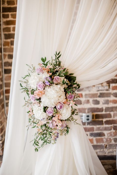 This gorgeous tie back for a spring wedding is filled with hydrangeas, lavender roses, peach stock, wax flower and ruscus. Pipe and drape ceremony flowers, lavender and pink wedding flowers, pastel wedding flowers  Lisa Foster Floral Design   www.lisafosterdesign.com Curtain Window Ideas, Lavender And Pink Wedding, Dusty Rose Wedding Theme, Curtains Embroidery, Peach Stock, Lavender Curtains, Wedding Flowers Pastel, Rose Wedding Theme, Bridal Colors