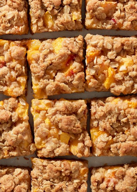 A close up of peach crumble bars lined up on a parchment paper background. Peach Oatmeal Breakfast Bars, Peach Breakfast Bars, Gluten Free Peach Crumble Bars, Mini Peach Crumble, Peach Oat Crumble, Peach Oat Bars, Peach Bars Oatmeal, Peach Oatmeal Bars, Peach Crumb Pie