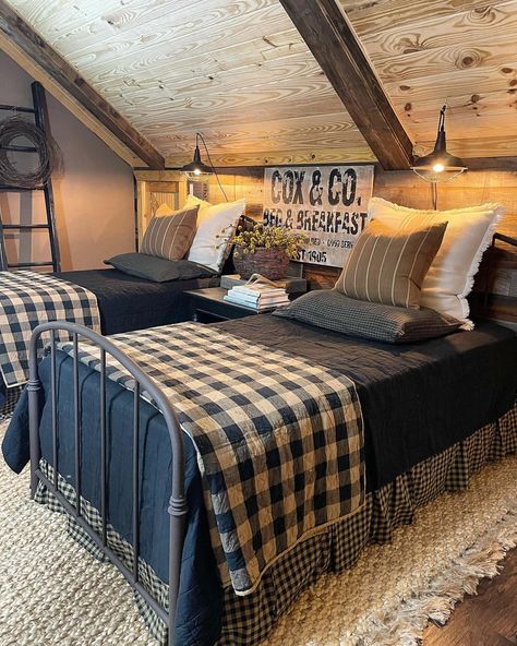 Two blue metal twin beds are pushed against a wood shiplap bedroom wall. Blue, beige, and white pillows are strewn at the head of the bed. Blue bedspreads cover the beds underneath folded blue and white checkered quilts laid at the foot of the bed. The checkered bed skirt hangs down to the white rug sitting on the warm wood floor. Navy Blue Country Bedroom, Bedding For Cabin, Outdoorsy Guest Bedroom, Twin Beds Guest Room Farmhouse, Quilt Bedspread Ideas, Blue Buffalo Check Bedroom, Masculine Farmhouse Bedroom, Blue Country Bedroom, Blue Plaid Bedding