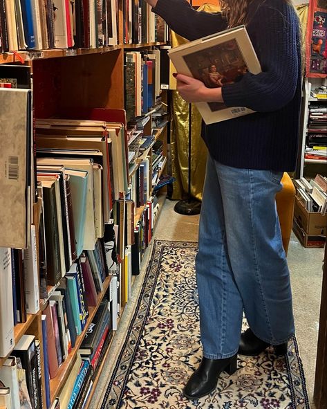 girl in blue jeans, blue sweater, and black boots with long brown hair looking at a bookcase full of old books in a cozy bookstore. bookstore full of pretty vintage books. cozy winter aesthetic. fall reading aesthetic. Bookstore Fall Aesthetic, Cozy Library Outfit, English Autumn Outfits, Bookstore Selfie, Cozy Pictures Aesthetic, Cool Fall Aesthetic, Bookseller Aesthetic Outfit, Autumn Manifestation, Frazzled English Woman Aesthetic