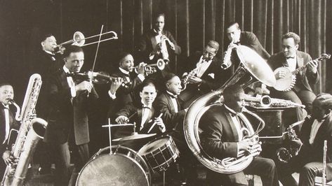 We see a band with some well-known instruments like drums and trombone. They make music that is called Jazz. It became very popular around the 1920s. The men wear neat suits. In the 1920s there were a lot of clubs, lounges and theaters in Chicago which played Jazz music, it was the new trend. It is believed that Jazz made its way through Chicago from New Orleans in 1915. Jazz is a mix of African and European musical traditions that started in the United States by african migrants form the west. Jelly Roll Morton, Violin Accessories, Chicago History Museum, Electric Violin, Popular Bands, Jazz Artists, Jazz Band, Jazz Club, Jazz Age