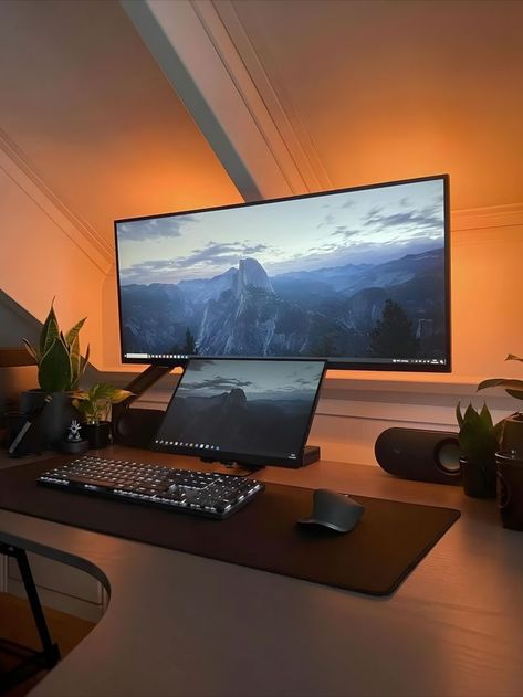 Home office featuring a wide monitor displaying a mountain landscape wallpaper, surrounded by warm orange lighting that creates a cozy ambiance. The desk holds a mechanical keyboard, a mouse pad, a laptop, and small potted plants, all under a gentle light. Portable Monitor Setup, Spare Bedroom Office Ideas, Ultrawide Setup, Workstation & Cubicle Accessories, Cozy Desk Setup, Gaming Computer Room, Minimalist Bedroom Furniture, Travel And Work, Cozy Desk