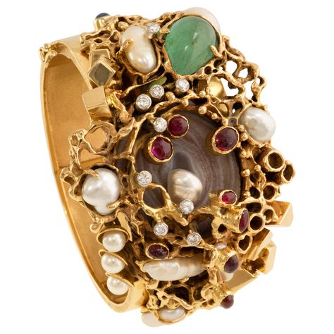 A cuff bracelet by Karl Stittgen circa 1970 featuring druzy agate, cabochon rubies, emeralds and sapphires, baroque and round white pearls, made in 18k yellow gold. The diamonds total approximately 0.50 carats and are H-I color and VS-SI clarity. Signed 'STITTGEN 18K' on the interior, hinged closure measuring 6.25" circumference. Karl Stittgen's design sensibility is wholly original, consisting of fine polished metalwork often with molten textures layered with gems gathered in vivacious cluster effects. Some of his jewels are highly architectural - as seen in his single stone rings - while others are made in an organic style. Stittgen arrived in Vancouver from Germany in 1952, and established himself as a watchmaker, jeweler and a key player in the very active artistic scene in Vancouver. Store Inspiration, Vintage Cuff Bracelet, Gold Cuff Bracelet, Single Stone Ring, Gold Armband, Agate Cabochon, Ruby Emerald, Gold Bracelet Cuff, Gold Cuffs