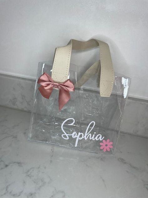 Beautiful clear PVC personalised gift bags with leather look double handles Perfect for a special birthday or celebration for a gift or party bag Size guide: 20 x 10 x 17 cm Personalised with any name Can also be changed to any other wording or message Font and colour of text can also be changed, and we have other colour options of the bow, if not noted at time of order then the pictured font will be used  ... daha fazla Clear Gift Bag Ideas, Bag Size Guide, Clear Gift Bags, Plastic Gift Bags, Small Business Packaging Ideas, Custom Party Favors, Teachers Day Gifts, Personalized Gift Bags, Wrapping Party