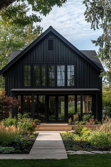 Modern barndominium house facade of black stained wood with black trim beautiful farmhouse garden landscape. Check out the coolest dark barndominium houses that combine rustic charm with modern sophistication, enhancing a living space with bold hues and sleek designs. Dark Exterior Cabin, Charcoal Grey Barndominium, Black Exterior Railing, Charcoal Siding House Exterior, Black Timber House, Board And Batten Siding Exterior, Dark Barndominium, Black Ranch House Exterior, Black Houses Exterior