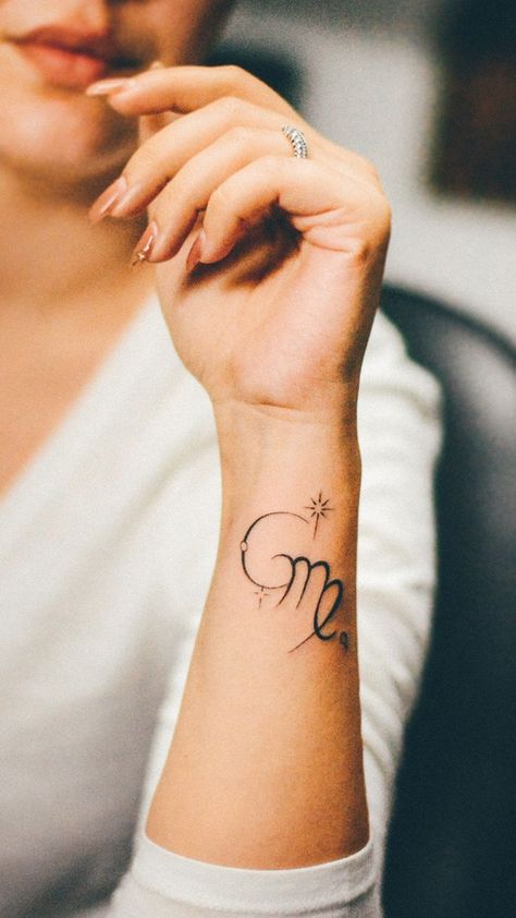 A woman's forearm is adorned with a delicate tattoo of the Virgo zodiac sign. The design features a stylized 'M' with a loop, representing the maiden, and is embellished with a small heart and twinkling stars, suggesting a personal connection to the celestial theme. Virgo Tattoo Ideas For Women, Rose Tattoo Simple, Simple Traditional Tattoo, Butterfly And Rose Tattoo, Virgo Tattoo Ideas, Virgo Sign Tattoo, Tattoo Simple Design, Virgo Tattoo Designs, Virgo Symbol