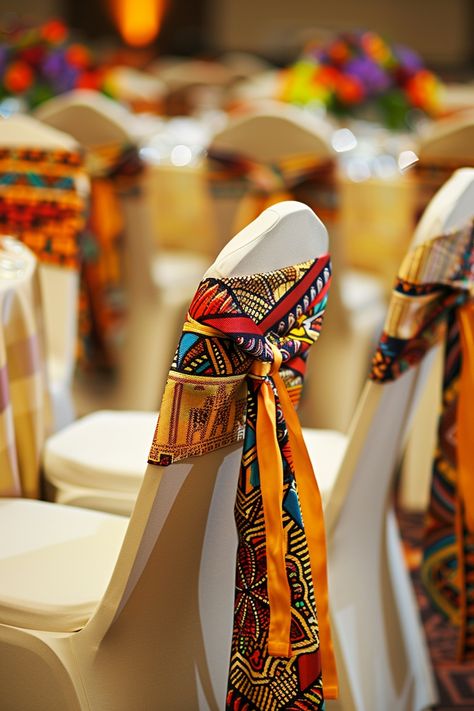 Transform your wedding venue into a cultural haven with vibrant Kente cloth chair sashes. Perfect for an Afrocentric celebration, these sashes add a touch of heritage and style. 🌍💒🎉 Celebrate love with a traditional twist! #WeddingInspiration #AfricanWedding #KenteDesign #WeddingDecor #AfrocentricWedding #CulturalElegance #ChairSashes #WeddingDetails African Centerpieces Ideas, African Traditional Wedding Decoration Table Settings, African Centerpieces, Gala Decorations, Wedding Chair Sashes, Centerpieces Ideas, Adinkra Symbols, African Home Decor, Kente Cloth