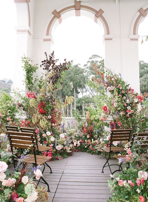 dramatic floral installation wedding ceremony backdrop with colorful flowers and bistro chairs Ceremony Flower Backdrop, Wild Flower Installation, Ceremony Floral Arrangements, Whimsical Ceremony, Wedding Flower Backdrop, Jewish Wedding Chuppah, Floral Pillars, Installation Wedding, Floral Arches