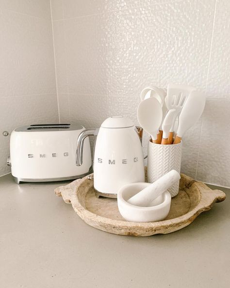 You'll love this kitchen corner featuring a decorative round wood tray placed on a gray countertop. The countertop is fitted against a gray tile backsplash. Decorate like a professional with stylish white kitchen utensils and appliances arranged in the corner. Kitchen Appliance Ideas, Kitchen Counter Corner, Gold Kitchen Utensils, White Kitchen Utensils, Beige Kitchen Cabinets, Concrete Kitchen Island, Gray Tile Backsplash, White Refrigerator, White Kitchen Appliances