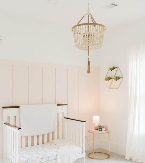 A white and pale pink nursery includes a board and batten wall behind a crib accessorized with blankets and a patterned mattress. A beaded chandelier hangs above the room that includes a gold metal side table and wall art. Pink Board And Batten Wall, Sherwin Williams Intimate White, Pink Board And Batten, Intimate White, Blush Pink Paint, Pink Painted Walls, Nursery Paint Colors, Grown Up Bedroom, Sherwin Williams White