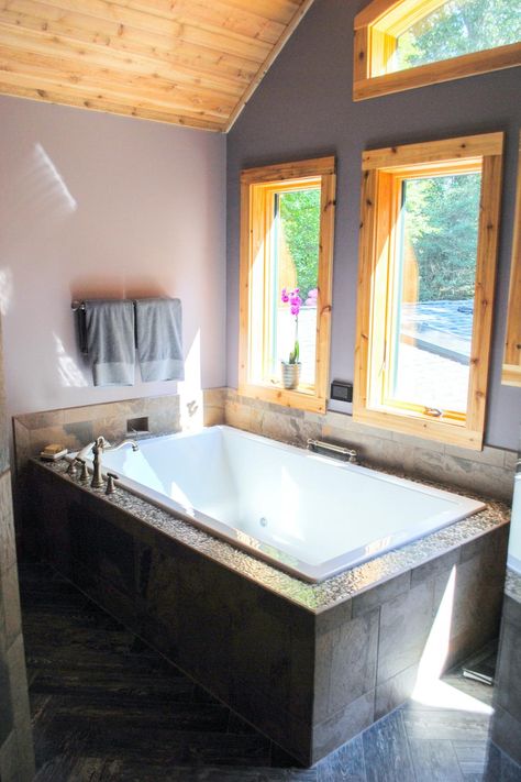 A luxurious two-person bathtub rests under a wall of windows in this rustic master bathroom. The beautiful wood-trimmed windows offer natural light and stunning views for a relaxing bathing experience. Two Person Bathtub, Bath Tub For Two, Two Person Tub, Rustic Master, Wood Look Tile Floor, Big Bathtub, Dream Bathtub, Large Bathtub, Grey Wall Color