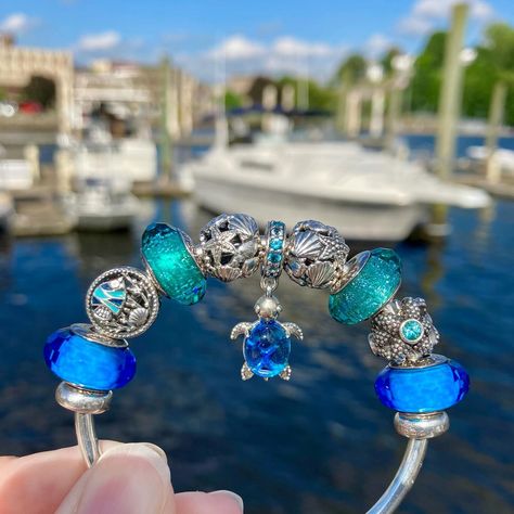 Happy Wednesday dear Pandora sisters!💙🩵💚😎 Today’s Ocean themed Pandora design at the Chelsea Harbor Marina features the lovely “Murano Glass Blue Sea Turtle” dangle charm as my centerpiece.🌊🛥️🐢 Included in my design are vintage classics from the Pandora Summer 2013 Collection, including a pair of the “Fascinating Aqua” muranos and the stunning silver “Sea Star”.💙🌊✨ I completed my styling with a pair of “Teal Shimmer” muranos, the “Ocean Life” charm and a pair of the silver Openworks with S... Pandora Ocean Charms, Pandora Ocean, Pandora Summer, Pandora Design, Blue Sea Turtle, Pandora Bracelet Charms Ideas, Pandora Murano, Pandora Bracelet Designs, Silver Sea