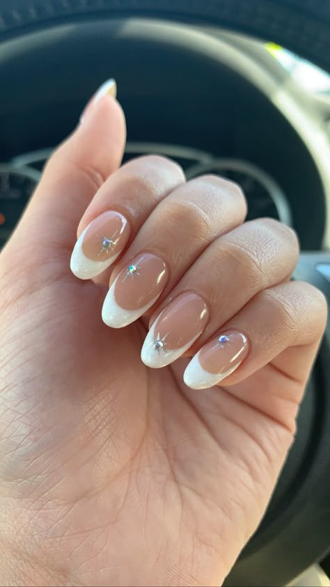 Almond shaped nails with a white glitter color. Chrome twinkle design with translucent gems in the center of the twinkles. White And Gem Nails, French Tip Gel Nails With Rhinestone, Nails Confirmation, Nails With Ringstones, Oval Nails With Gems, Chrome Nails With Diamonds, Chrome Nails Gems, Frenchies With Gems, French Nails With Crystals