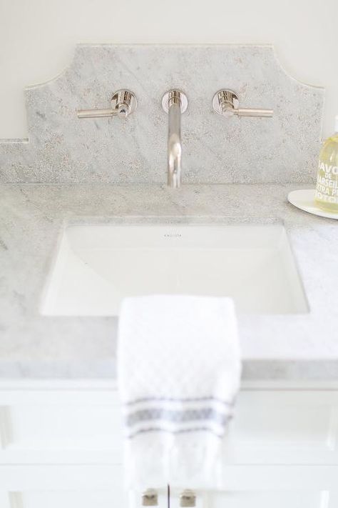 A polished nickel faucet is mounted to a curved marble backsplash above a Kallista sink fixed to a gray marble countertop complementing a white bath vanity. Marble Backsplash Bathroom, Polished Nickel Faucet, Wall Faucet, Bathroom Lamp, Wall Mount Faucet Bathroom, Stone Backsplash, Transitional Bathroom, Marble Backsplash, Wall Mount Faucet