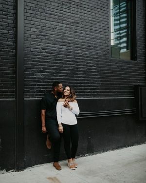 Couple-resting-against-a-black-brick-wall-in-Austin-TX-for-their-outdoor-engagement-photoshoot Engagement Photos With Brick Wall, Brick Wall Engagement Pictures, Winter Engagement Photos With Dog, Anniversary Photography Poses, Sitting In The Park, Anniversary Photography, Wedding Anniversary Photos, Urban Engagement, Engagement Photography Poses