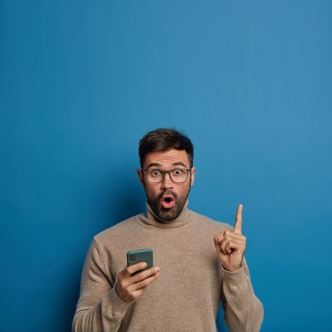 Surprised unshaven man holds phone, show... | Free Photo #Freepik #freephoto #man-smartphone #man-phone #amazed #pessoa-celular Man Holding Phone, Man Background, Man Pointing, Brown Jumpers, Poppy Pods, Brown Jumper, Classy Suits, Vertical Images, Business Photoshoot