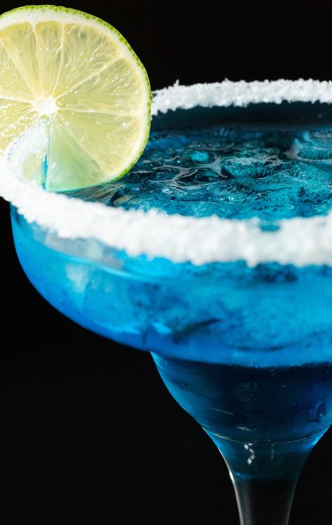 A tall margarita glass has a salt rim and is filled with crushed ice and a light blue margarita. It is garnished with a lime wheel. Blue Margaritas, Elegant Cocktails, Blue Curacao Liqueur, Blue Margarita, Best Drink Recipes, Fun Drink Recipe, Beverage Ideas, Tequila Cocktail, Best Cocktails