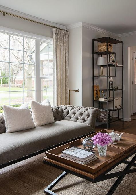 A gray tufted sofa accented with white pillows sits on a jute rug in front of windows dressed in gray floral curtains. Sofa In Front Of Window, Couch In Front Of Window, Grey Tufted Sofa, Light Gray Couch, Chunky Jute Rug, Living Room Redesign, Jute Rug Living Room, Organic Living Room, Jute Wool Rug