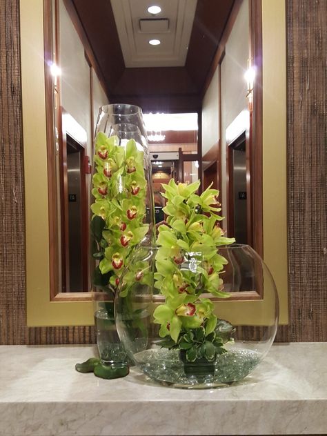 Modern glass design with green cymbidium orchids Cymbidium Orchids Arrangement, Wedding Alter Flowers, Tall Vase Arrangements, Hotel Flower Arrangements, Alter Flowers, Wedding Alter, Tropical Centerpieces, Hotel Flowers, Office Flowers