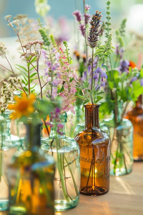 Elevate your wedding decor with a unique touch of the past. These vintage perfume bottles turned vases are filled with an array of herbs and wildflowers, perfect for a bohemian-themed celebration. 🌿🌼💐 A touch of nostalgia meets natural beauty for your special day. #WeddingInspiration #BohoWedding #CenterpieceIdeas #VintageDecor #FloralDesign #DIYWedding #EventStyling #WeddingFlowers Boho Wildflower Centerpieces, Wedding Table Wildflowers, Rustic Whimsical Wedding Theme, June Wedding Centerpieces, Thrifted Wedding Centerpieces, Wedding Wildflower Theme, Wildflower Wedding Table Decor, Cottagecore Aesthetic Wedding, Wildflower Wedding Flowers