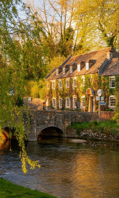 A period property in the evening sunshine behind a river and small road bridge. The spring scene is surrounded by trees that are beginning to bloom. England Aesthetic, England Countryside, Cotswolds England, Castle Combe, Voyage Europe, Dream Travel Destinations, The Cotswolds, English Countryside, England Travel