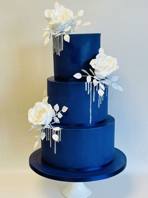 Selena, dramatic navy blue wedding cake with silver drip and statement white sugar rose sprays Debut Cake 18th Elegant Blue, Royal Blue Wedding Cakes Elegant, Navy Blue And Purple Wedding Cake, Navy Blue White And Gold Wedding Cake, Navy Blue Cake Ideas, Royal Blue And Silver Cake, Blue And Black Cake, Wedding Cake Royal Blue, Navy Wedding Cakes