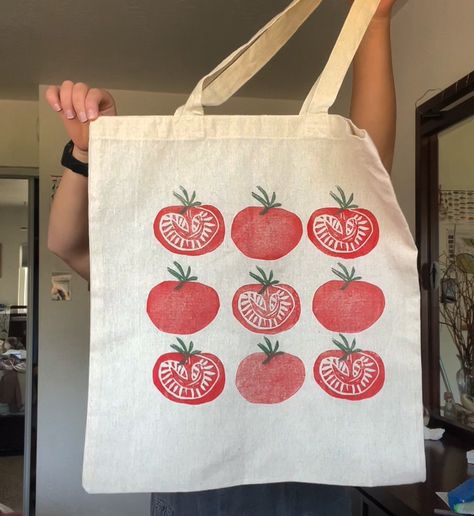 I am holding a tomato tote bag that I made. It is khaki/tan material with bright red tomatoes stamped onto it. Hand Printed Canvas Tote Bag, Rectangular Cotton Canvas Bag With Screen Print, Block Print Tote Bag, Lino Print Tote Bag, Screen Print Tote Bag For Shopping, Eco-friendly Screen Print Canvas Bag, Screenprinting Totebag, Textiles Projects, Printing Press