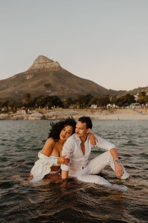 Engaged couple sitting in the water while holding each other. Lions Head is in the background, a famous mountain in Cape Town Sunset Photoshoot Ideas Couple, Africa Photoshoot, Couples Photoshoot Sunset, Black Couple Photoshoot, Sunset Prewedding Shoot, Cape Town Couple Shoot, Canyon Couple Photoshoot, Black Couple, Couple Photoshoot