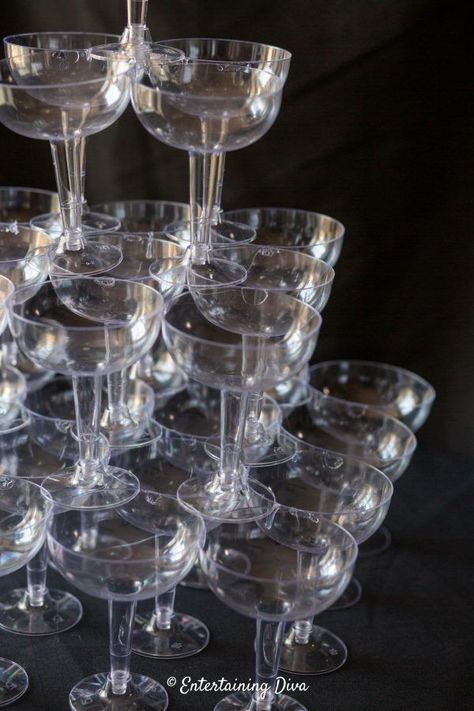 This DIY champagne glass tower is made from plastic coupe glasses that are glued together so it won't fall over or break! It makes a great centerpiece for a Great Gatsby party, roaring 20's event or speakeasy. #entertainingdiva #gatsbyparty #roaring20s #speakeasyparty #centerpiece #diypartydecor Champagne Fountain Diy, How To Make A Champagne Tower, Champagne Tower Diy, Roaring 20s Food, 1930 Party, Champagne Glass Tower, 1920 Wedding, Champagne Fountain, Plastic Champagne Glasses