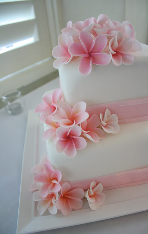 Two tier cake covered in fondant and decorated with sugar flower frangipanis Square Wedding Cakes Simple, Hibiscus Wedding Cake, Frangipani Cake, Fondant Hawaiian Flowers, Two Tier Tropical Wedding Cake, Wedding Cake Flowers Simple, Fondant Hibiscus Flowers Tutorial, Plumeria Wedding Cake, Wedding Cake With Fondant