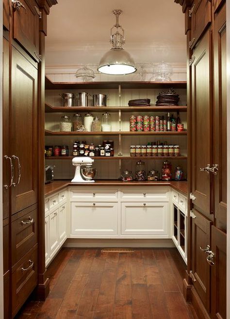 U shaped white and brown cottage kitchen pantry is lit by a Country Industrial Pendant hung over dark stained rustic wood floors accenting facing dark stained paneled refrigerators positioned on either side of white cabinets finished with a wood countertop positioned beneath beautifully organized wraparound wood shelves mounted on a beadboard trim. Brown Cottage, Kitchen Butlers Pantry, Pantry Inspiration, House Pantry, Rustic Wood Floors, Pantry Room, Butler’s Pantry, Pantry Remodel, Kitchen Pantry Design