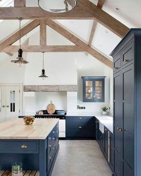 a navy kitchen with a white backsplash, countertops, a large island with a wooden countertop and wooden beams Navy Kitchen, Paint Trends, Becki Owens, Farmhouse Kitchen Island, White Backsplash, Rustic Kitchen Design, Classic Kitchen, Blue Cabinets, Rustic Kitchen Decor