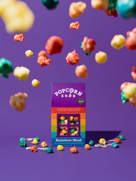 Commercial Product Photography For Popcorn Shed. Taking inspiration from the packaging's color scheme, we went for a purple backdrop which made the rainbow colored popcorn pop out even more. We added the textures of the popcorn to make it seem like a storm of colorful popcorn. #commercialphotography #productphotography Pop Color Photography, Summer Drink Ads Creative Advertising, Sweets Product Photography, Cereal Photoshoot Photo Ideas, Popcorn Product Photography, Packaging Photography Ideas, Candy Photography Food Styling, Packaged Food Product Photography, Candy Product Photography