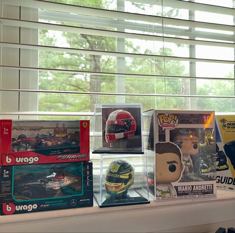 mini versions of a f1 Ferrari and Mercedes cars, lewis hamilton and Michael Schumacher helmet, and a funko pop Mario Andretti on a windowsill. Formula One Bedroom, F1 Inspired Room, F1 Bookshelf, F1 Shelf, F1 Bedroom, F1 House Decor, F1 Interior, F1 Funko Pop, Formula 1 Room Decor