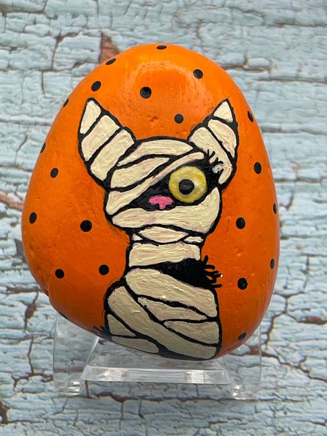 Mummy Cat with Glow in the Dark Eye, Halloween Art, Painted Rock, Stone Painting Measures approximately:  Height 2.75" Length 2" Depth .75" ✽ My painted rocks are natural creek rocks collected locally in middle Tennessee and hand painted by me.  ✽ Your stones are handpicked and hand painted by me with love! Each is a one-of-a-kind piece of art! I hope they bring much joy, happiness, and a smile to you.   ✽ These are natural creek rocks so each stone is unique and no two rocks are identical.  The size, shape, and texture may vary slightly. ✽ Each stone design is drawn by hand, painted with acrylic paints, sealed, and packaged with care to send to your home from my home in middle Tennessee.   ✽ All my creations are sealed to protect and preserve the quality. ✽ Want a custom design?  If you d Fun Halloween Art Projects, Fall Rock Art Ideas, Mummy Painted Rocks, Painted Halloween Rocks, Halloween Painted Rocks, Fall Rock, Halloween Kunst, Diy Rock Art, Art Pierre