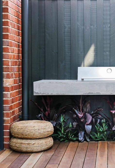 An outdoor kitchen with a barbecue creates a walkway between the house and the studio apartment. The palette of concrete, red brick and black wood continues inside.