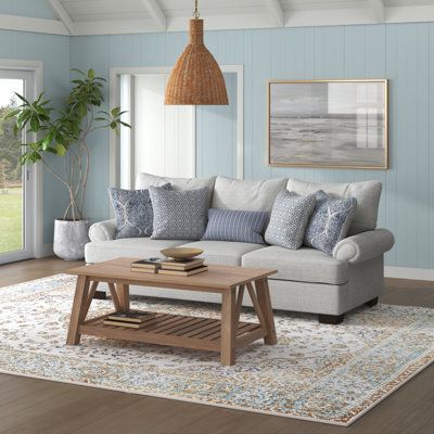 This sofa features a laid-back silhouette with roll arms and pillow backs to bring a hint of coastal farmhouse charm to your living room. It has a solid and engineered wood frame that sits on tapered legs with a dark brown finish. Wrapped with 100% polyester in a neutral gray tone, this couch is filled with foam and polyester and supported by sinuous springs to give you some padding as you relax. The seat and back covers are removable to make cleaning a cinch. Five vibrantly patterned toss pillo Grey Coastal Living Rooms, Coastal Casual Living Room, Coastal Farmhouse Living Room, Beach House Decor Living Room, Coastal Cottage Living Room, Hamptons Living Room, Coastal Sofa, Florida Living Room, Beachy Living Room