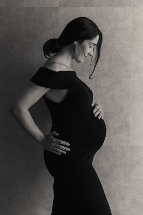 Stunning maternity photo of a mother who poses alone in a black dress. Indoor black and white maternity photoshoot. #maternityphotography #momposesalonematernity #blackandwhitematernityshoot Pregnancy Photo Shoot Outfits, Solo Pregnancy Photoshoot, Maternity Solo Poses, Solo Maternity Shoot, Maternity Photography Poses Alone, Solo Maternity Pictures, Maternity Photography Black Backdrop, Maternity Photoshoot Black And White, Maternity Photos Black And White