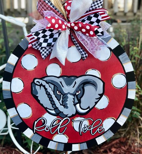 Show off your team spirit for the Alabama Crimson Tide with this adorable Big Al door hanger.  It is hand painted which makes this a one-of-a-kind creation.  The wood round measures approximately 18" and is made from 1/4" birch plywood.  A decorative bow and wire are attached for hanging which makes it between 24 and 26 inches tall.   Due to the handcrafted nature of this item, slight variations in paint colors and ribbon availability may occur.  If you have any specific color requests, please n Alabama Door Hanger, Alabama Crafts, Alabama Wreaths, Football Door Hangers, Big Al, Wood Door Hanger, Fall Door Hangers, Alabama Roll Tide, Wood Door Hangers