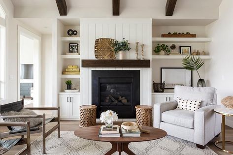 Asymmetrical white styled shelves fitted over white shaker cabinets flank a white shiplap fireplace accented with a chunky stained oak mantel topped with French candlesticks and a tobacco basket. Asymmetrical Fireplaces, White Fireplace Mantels, White Built Ins, Transitional Living Room Design, White Brick Fireplace, Living Room Built Ins, Shiplap Fireplace, Fireplace Built Ins, Cottage Living Rooms