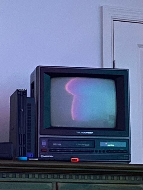 An 80s tube tv sitting on a wooden dresser, the screen is off and the reflection shows cool colored lights in the room. Next to it is a ps2, in front of it is a switch Old Tv Wallpaper, Tv Asthetic Picture, 2000s Tv Aesthetic, Old Television Aesthetic, 90s Tv Set, Games To Install On Your Phone, Vhs Tv Aesthetic, 80s Tv Aesthetic, Box Tv Aesthetic